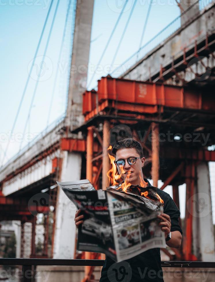 Guy reads a burning newspaper, in the background a bridge photo