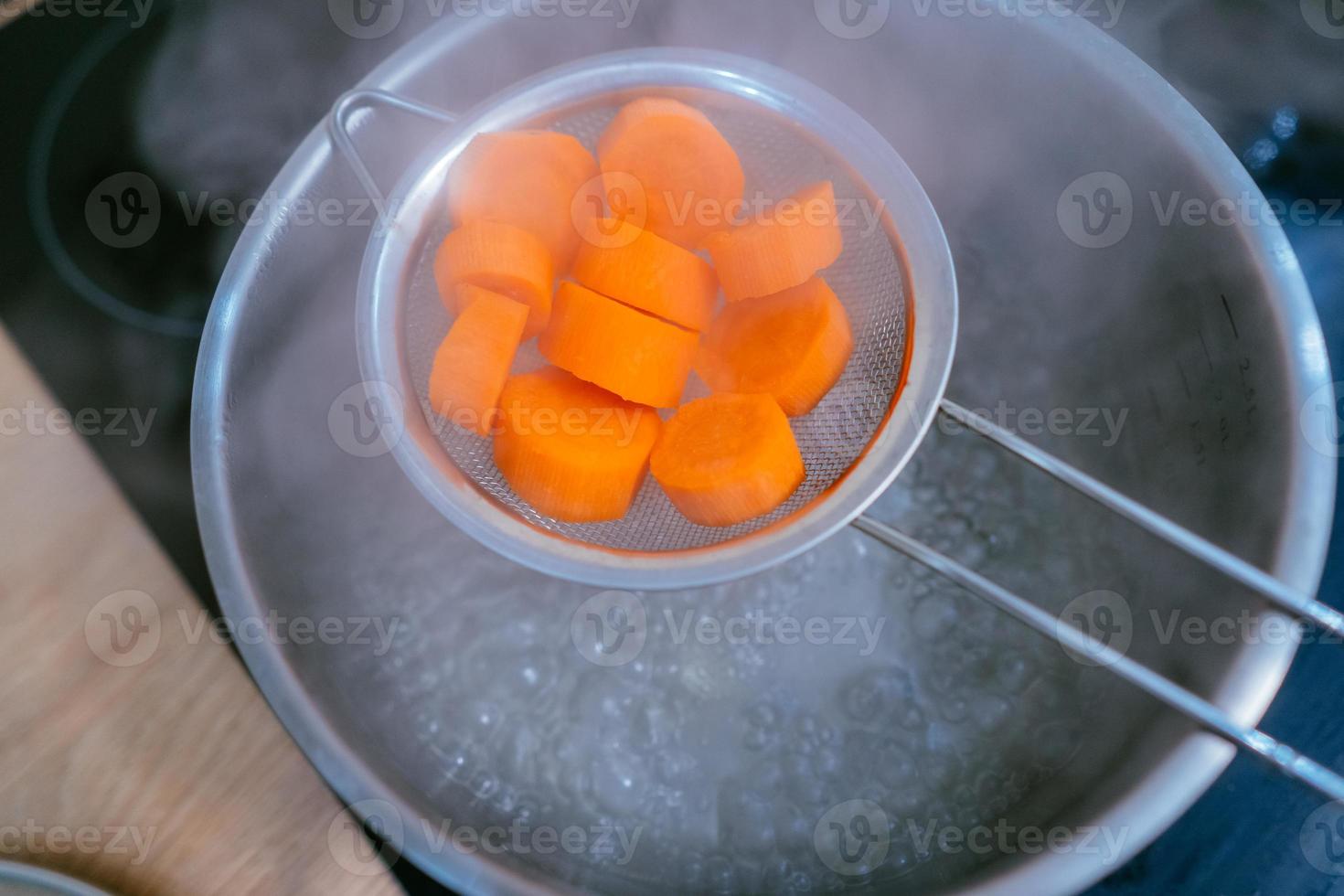 The image of a small amount of chopped carrots over a boiling pan photo