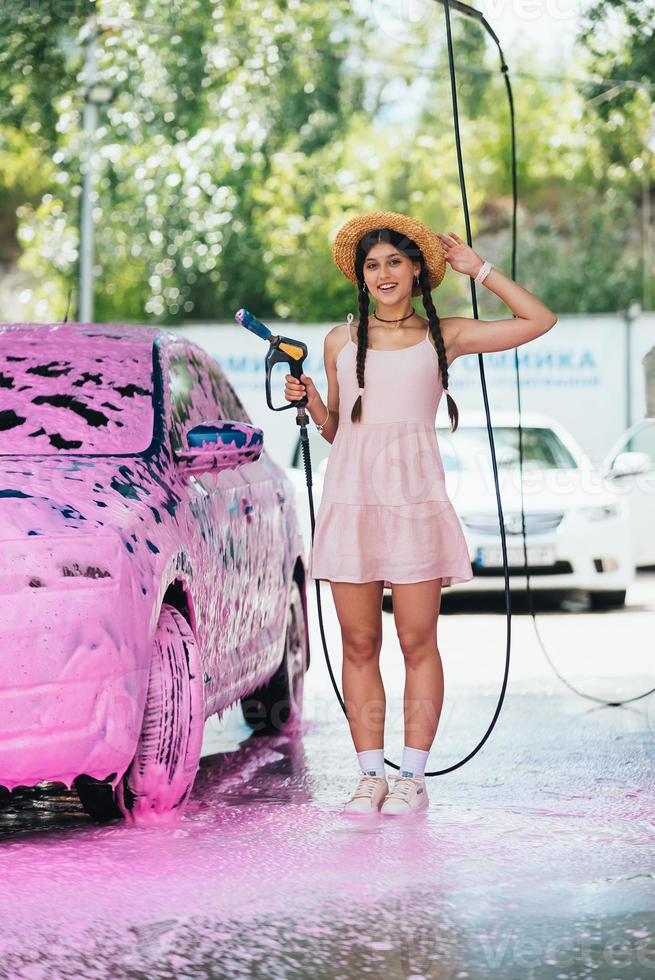 Woman with hose stands by car covered in pink foam photo