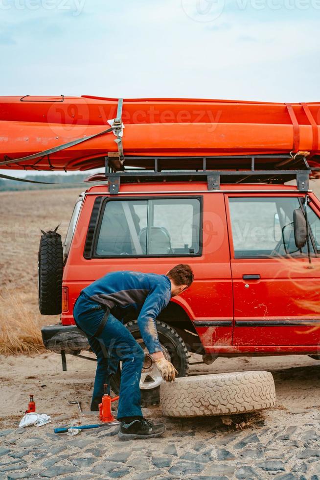 Man rolls a new replacement wheel to 4x4 off road truck photo