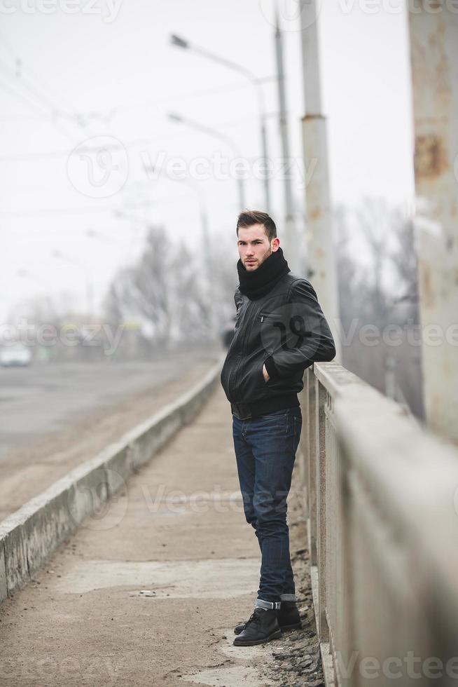 A man dressed in jeans and jacket stands near the main road in foggy weather photo