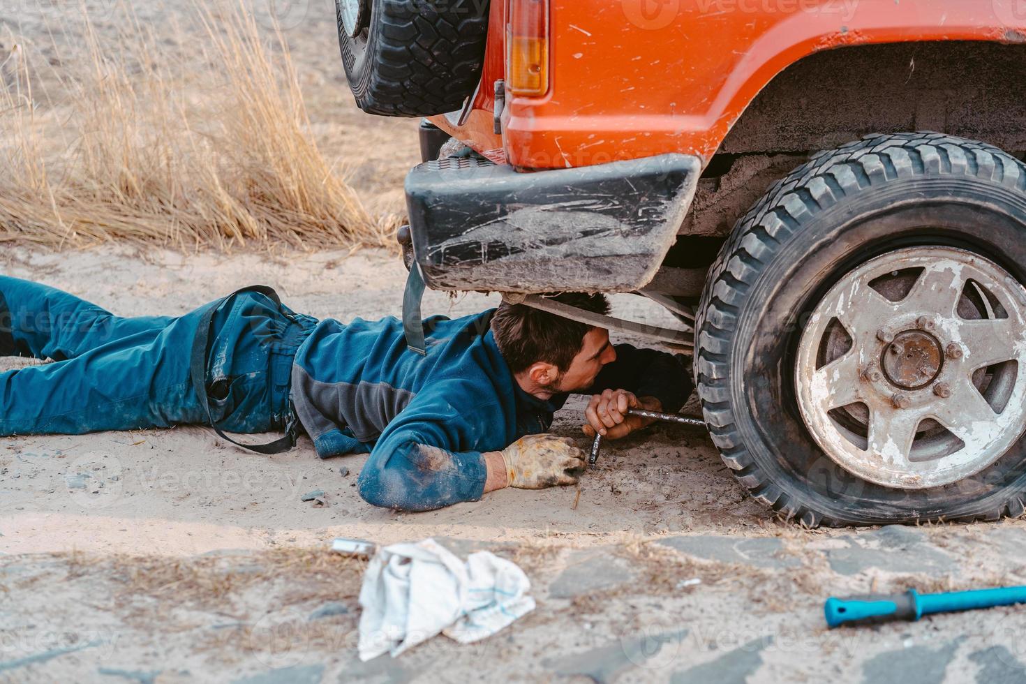 el hombre yace debajo de un camión 4x4 en un camino de tierra foto
