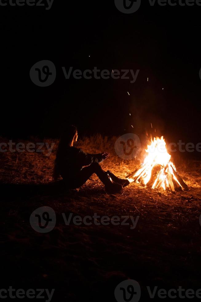 mujer sentada y calentándose cerca de la hoguera en el bosque nocturno. foto