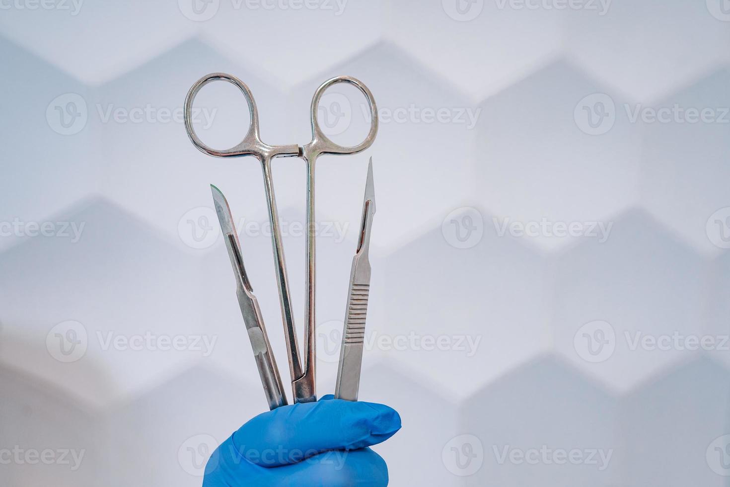 A rubber gloved hand holds two scalpels and a clamp photo