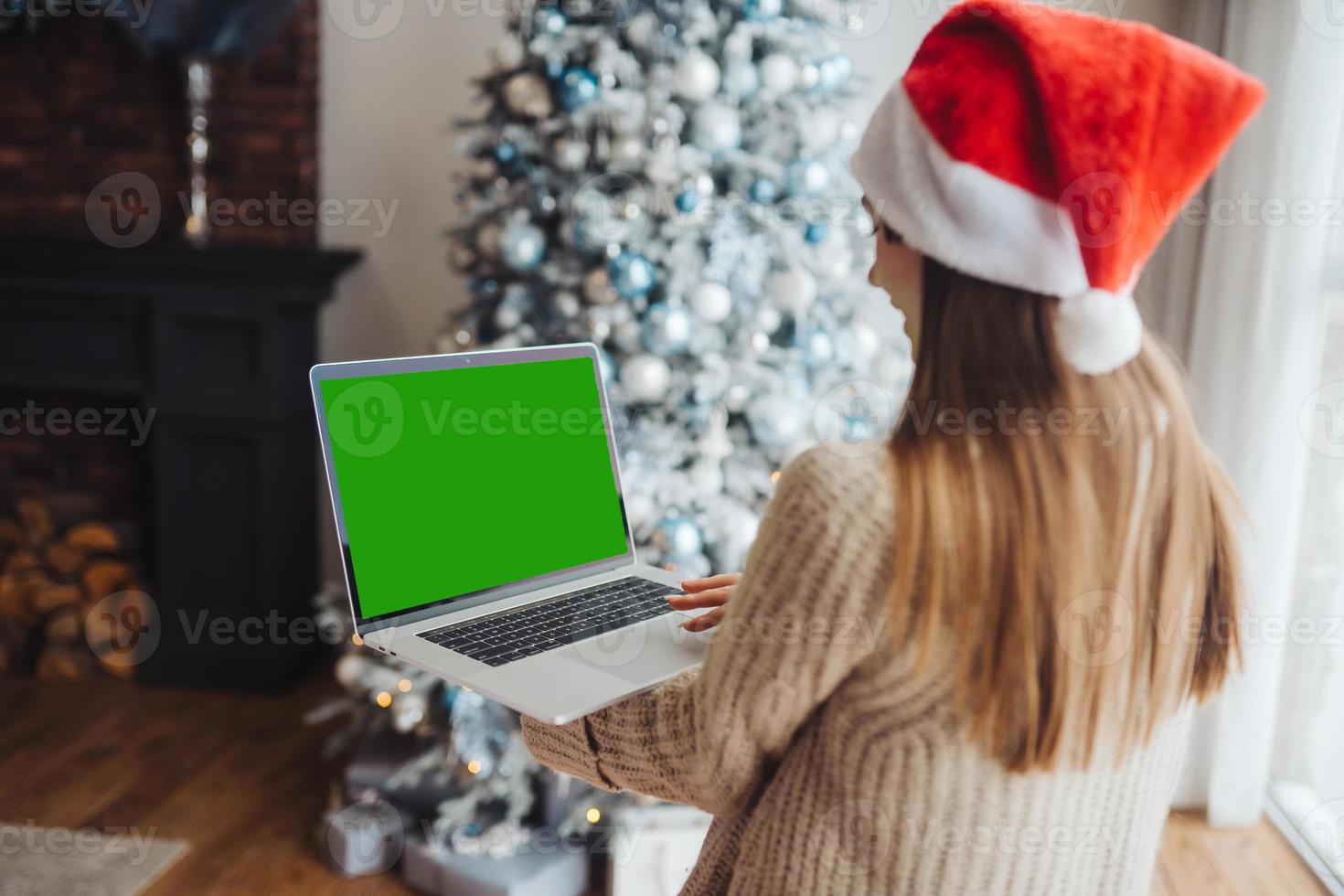 Female wearing santa hat while speaking with online friend on laptop photo