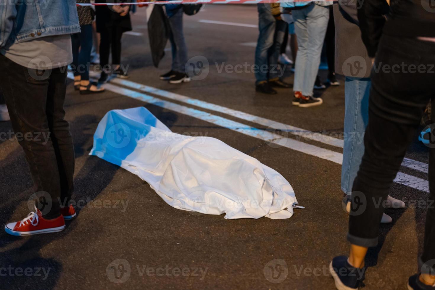 cuerpo humano cubierto por una sábana tirada en la calle. foto