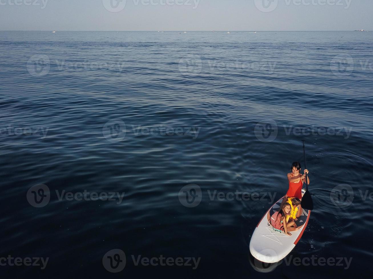 Mother with two daughters stand up on a paddle board photo