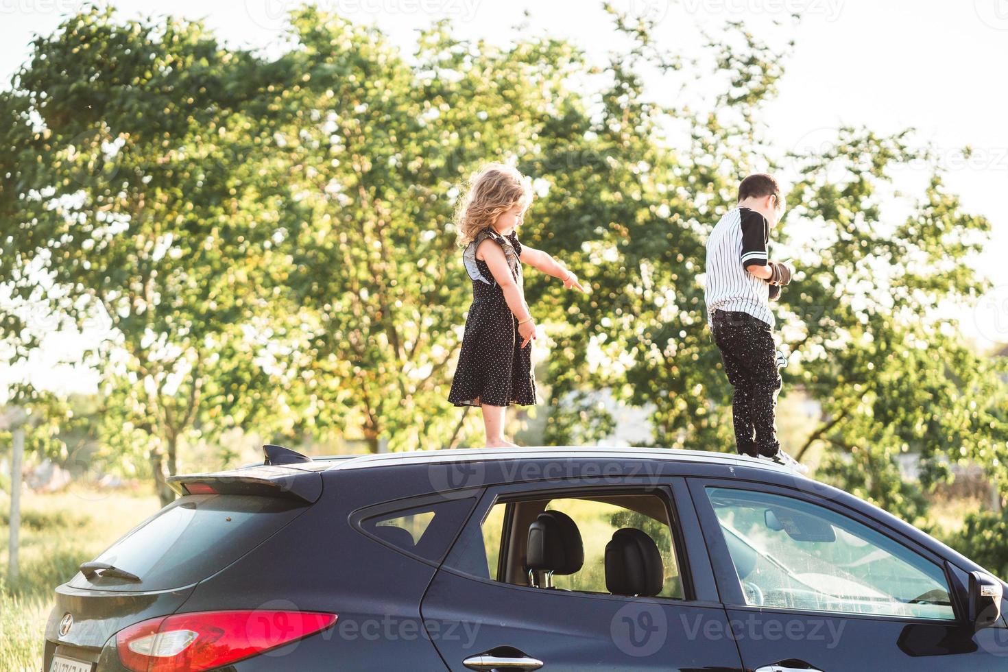 Two children stand on the roof of a car photo