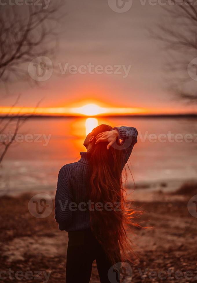 Woman enjoying time relaxing by the beautiful lake at sunrise. photo