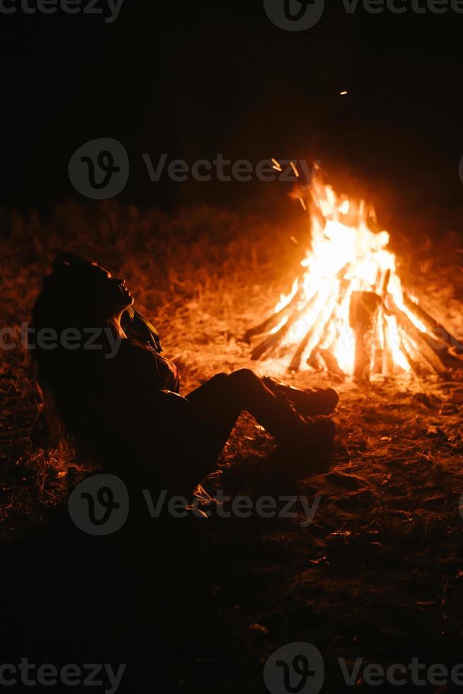 mujer sentada y calentándose cerca de la hoguera en el bosque nocturno. foto