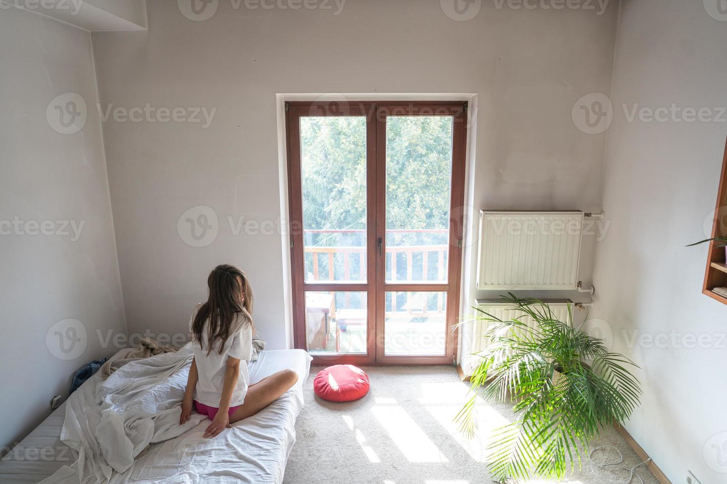 mujer joven sentada en la cama y mirando por la ventana. foto