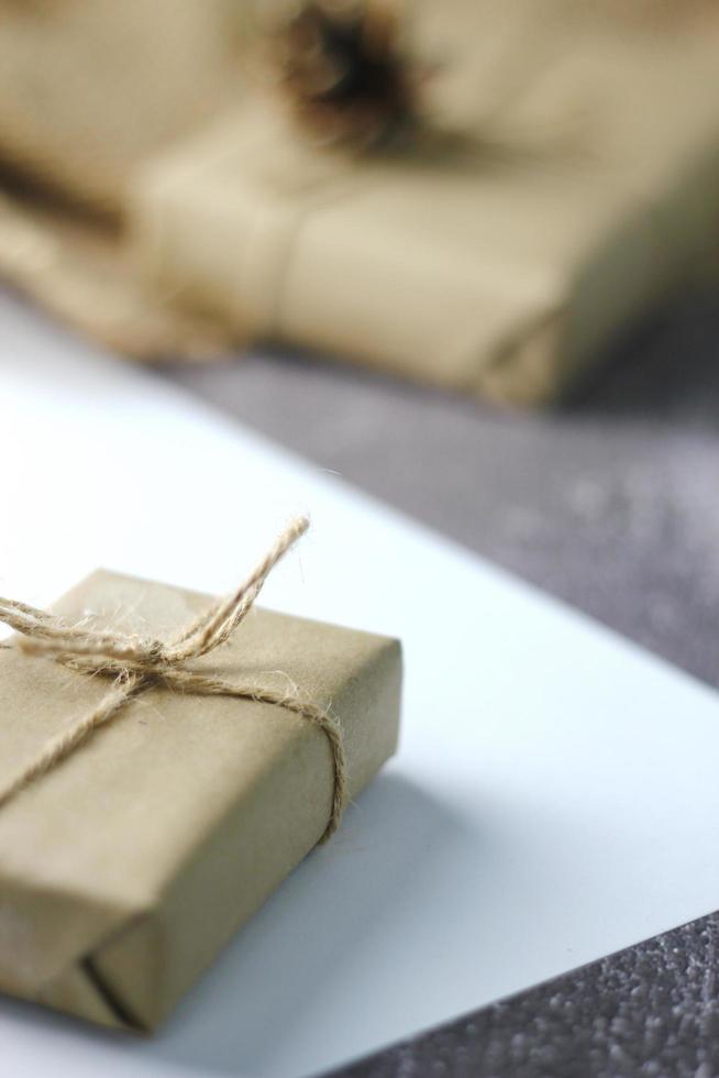 Holidays Gifts  Christmas and New Year Gift box wrapped in brown paper, pine cones and white paper and pens placed on the table, copy space. photo