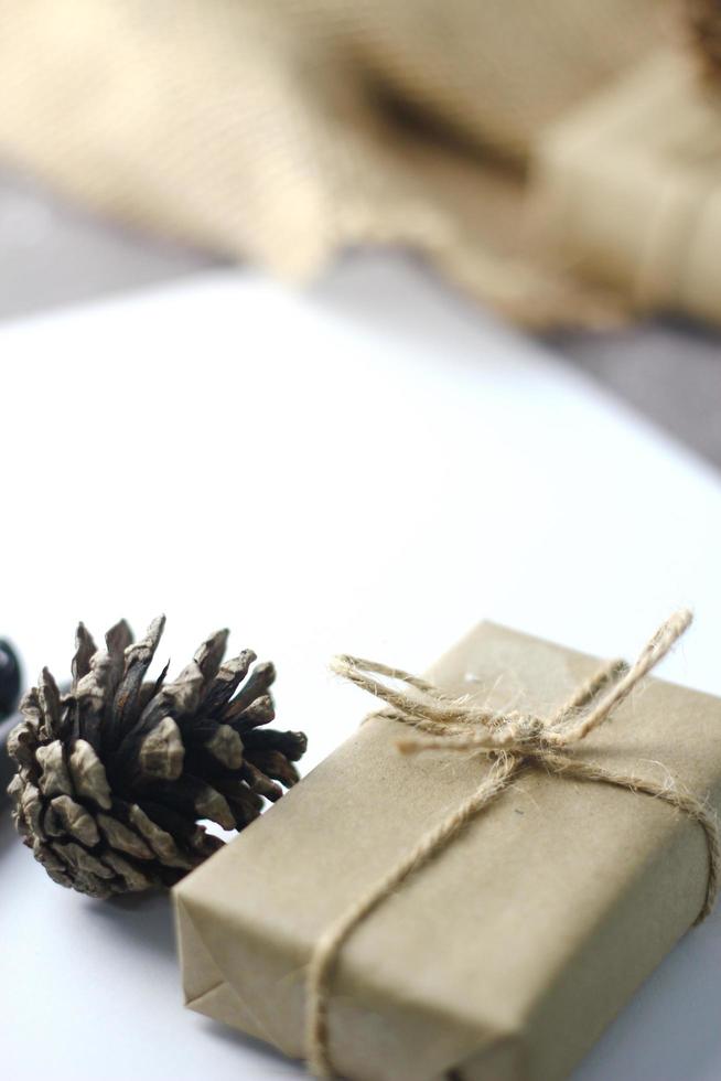 Holidays Gifts  Christmas and New Year Gift box wrapped in brown paper, pine cones and white paper and pens placed on the table, copy space. photo