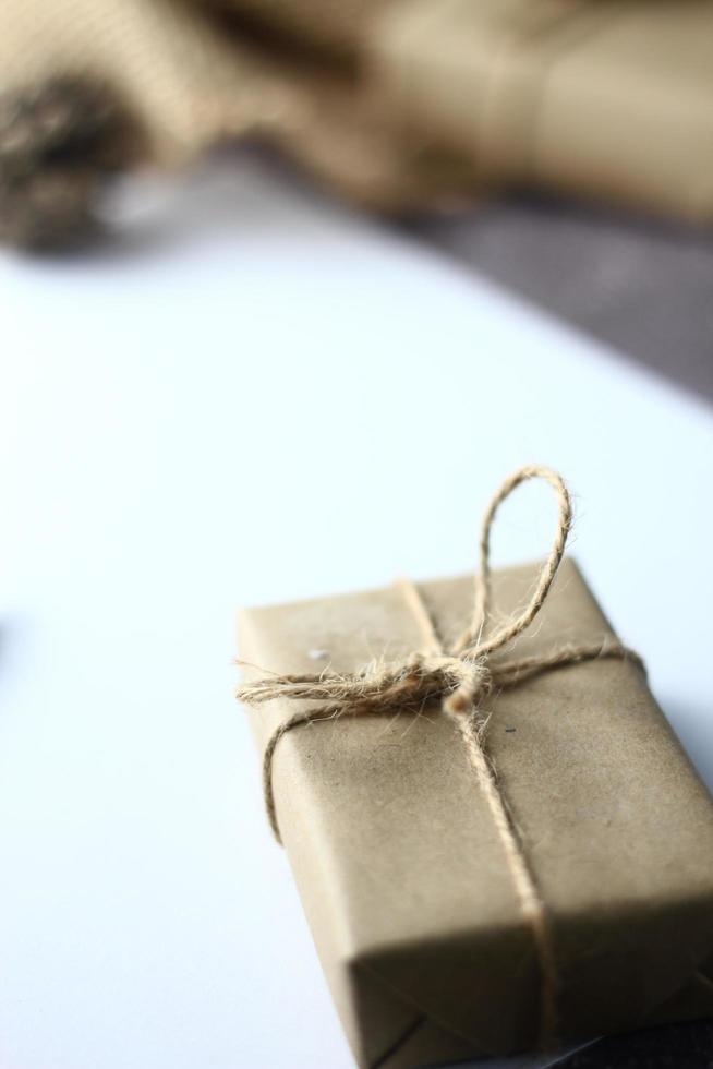 regalos de vacaciones caja de regalo de navidad y año nuevo envuelto en papel marrón, conos de pino y papel blanco y bolígrafos colocados sobre la mesa, copie el espacio. foto