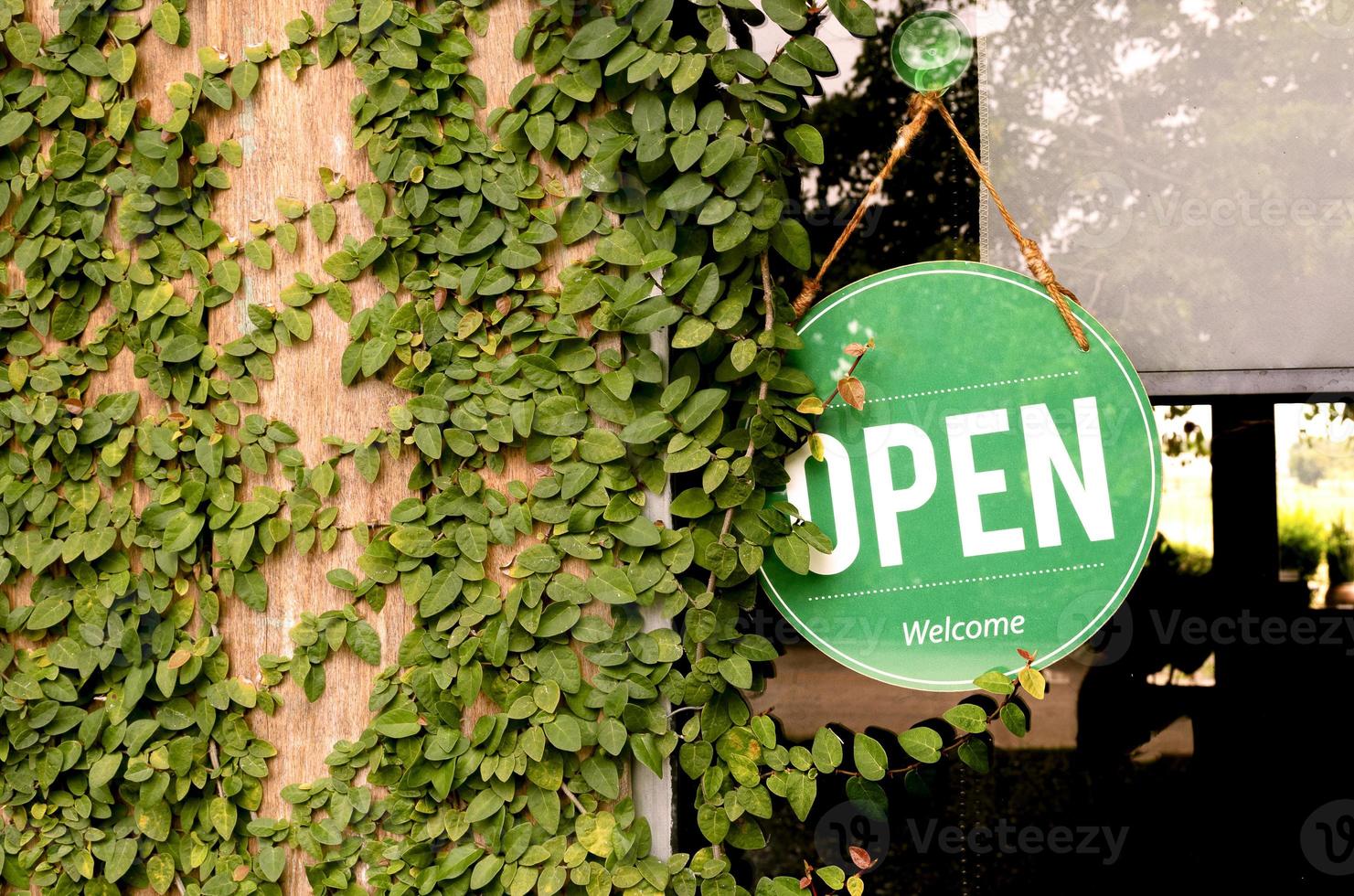 Hanging green sign with message OPEN on window with leaves ivy on wooden wall at coffee shop photo