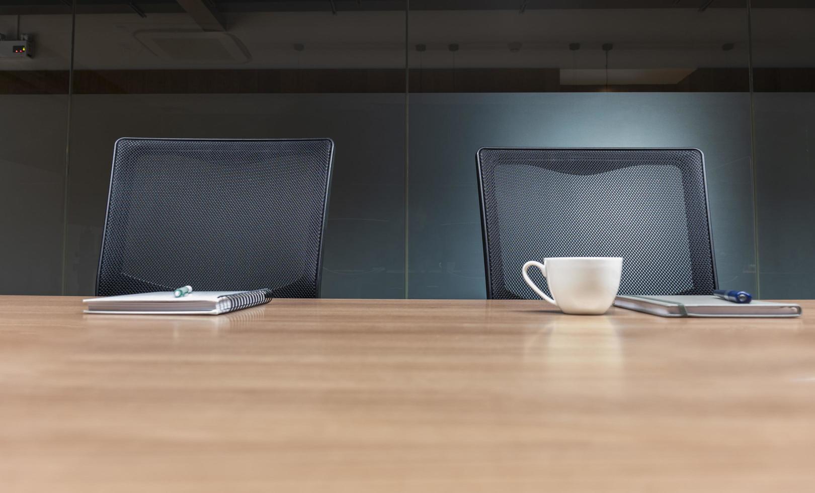 Coffee cup and notebook on table with two black armchairs in meeting room photo