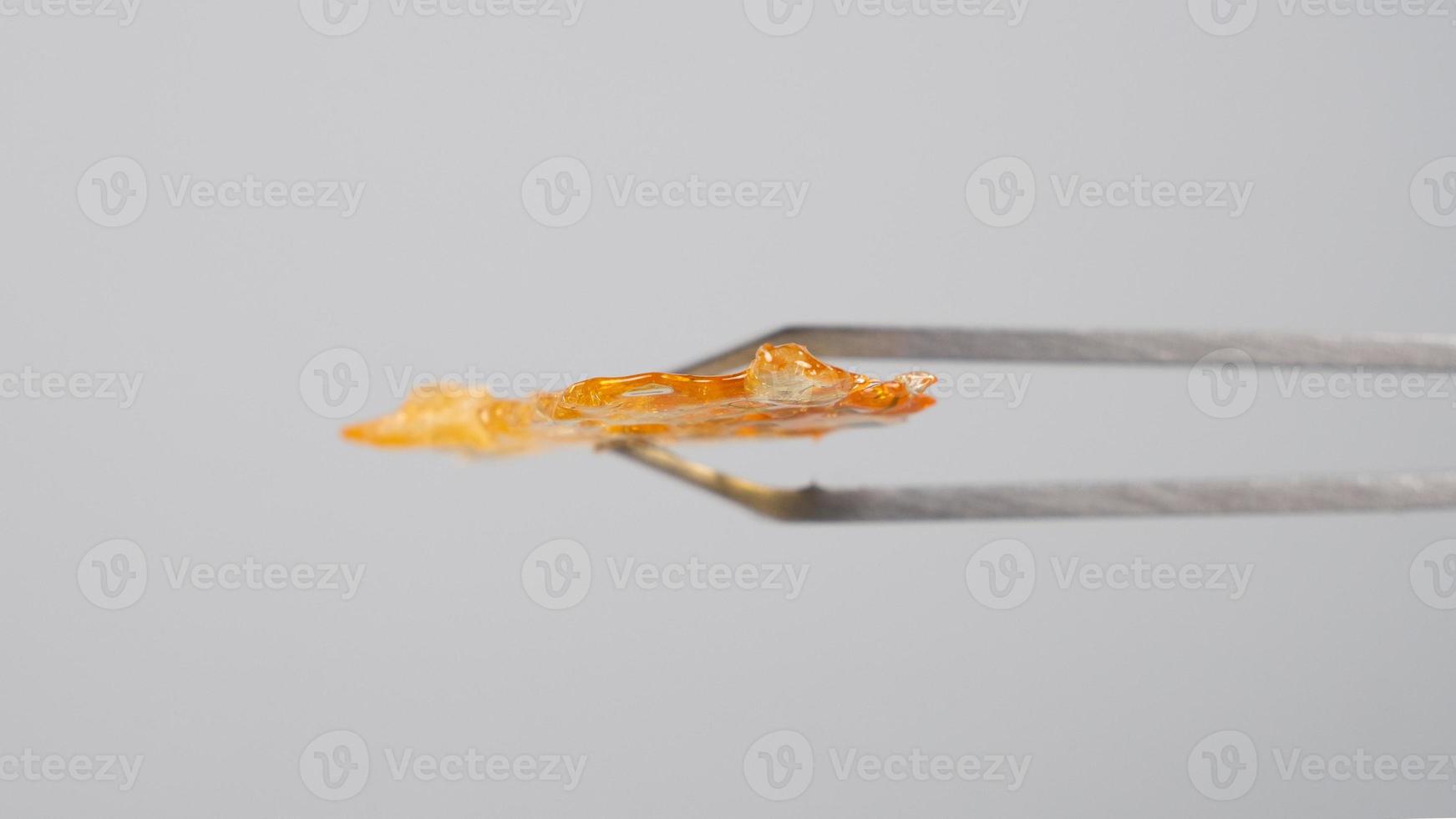 tweezers and piece of golden resin marijuana concentrate on gray