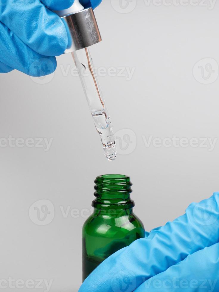 hand hold pipette with medicine oil in a bottle on gray background photo