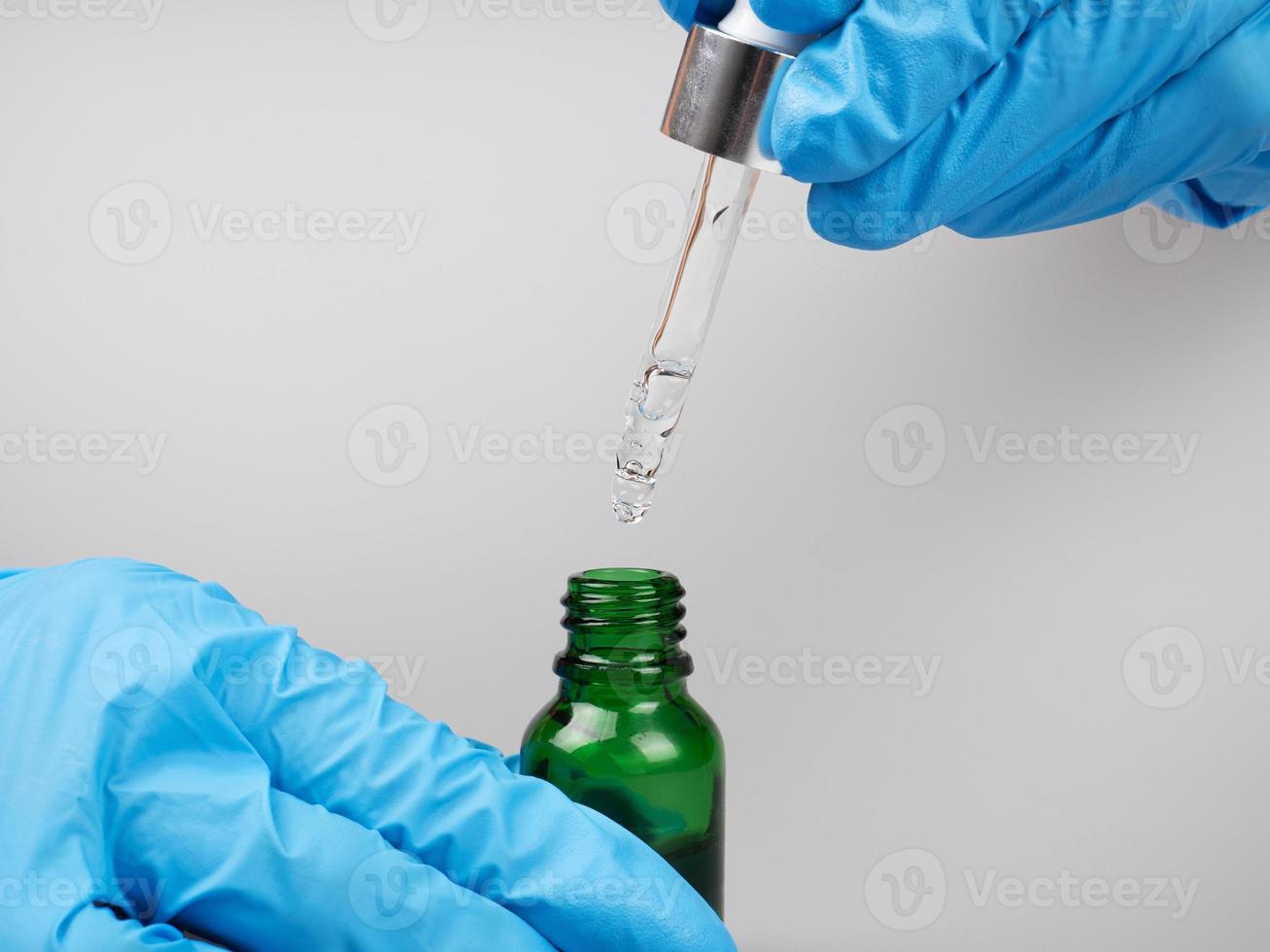 a doctor in gloves holds a pipette and a bottle of medicine in his hands photo