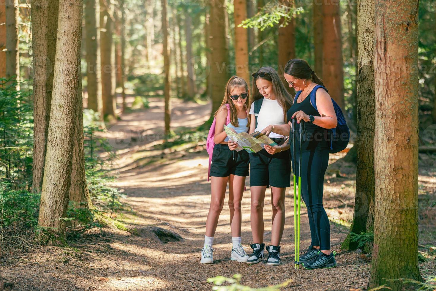 Forest path with female mountaineers reading a map. Teenage girls hold a map while a woman holds hiking poles photo