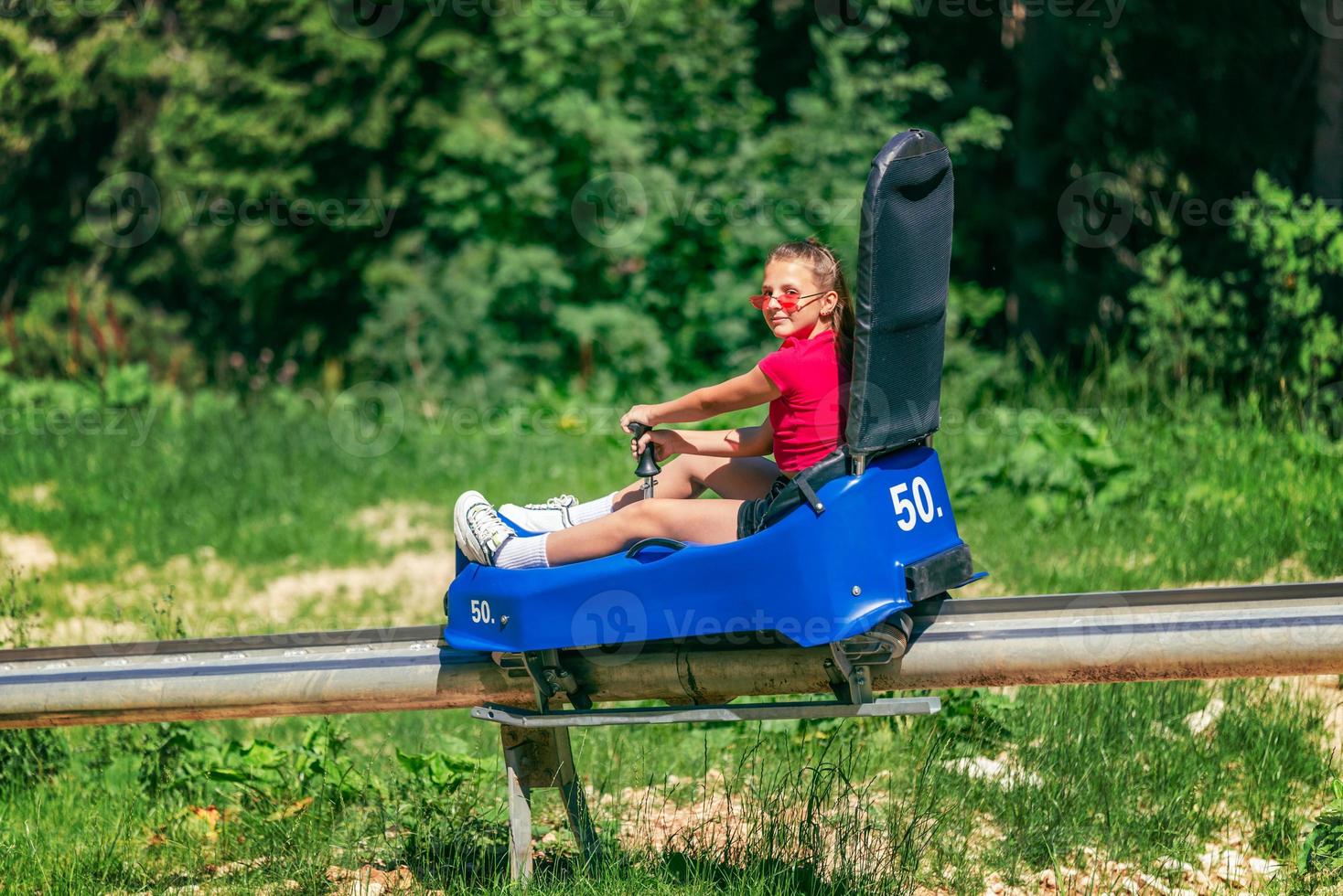 Girl go downhill ski slope on mountain roller coaster at summer. Summer tourism and fun on the mountain concept photo