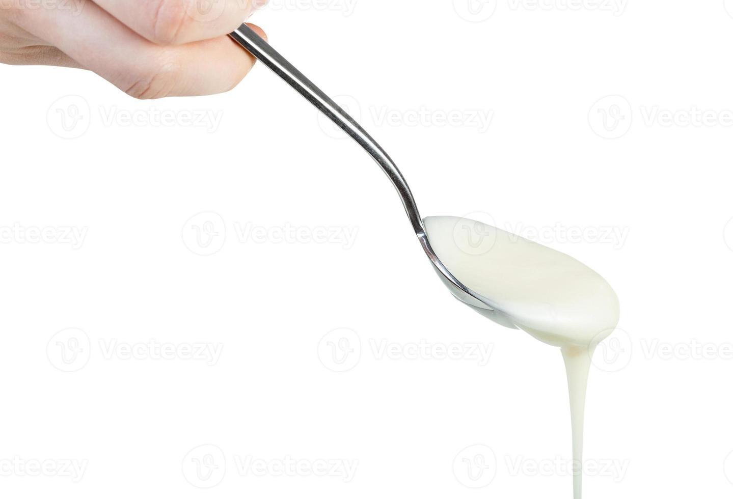 side view of white honey pouring from steel spoon photo