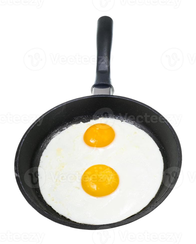 front view of two fried eggs in black pan isolated photo