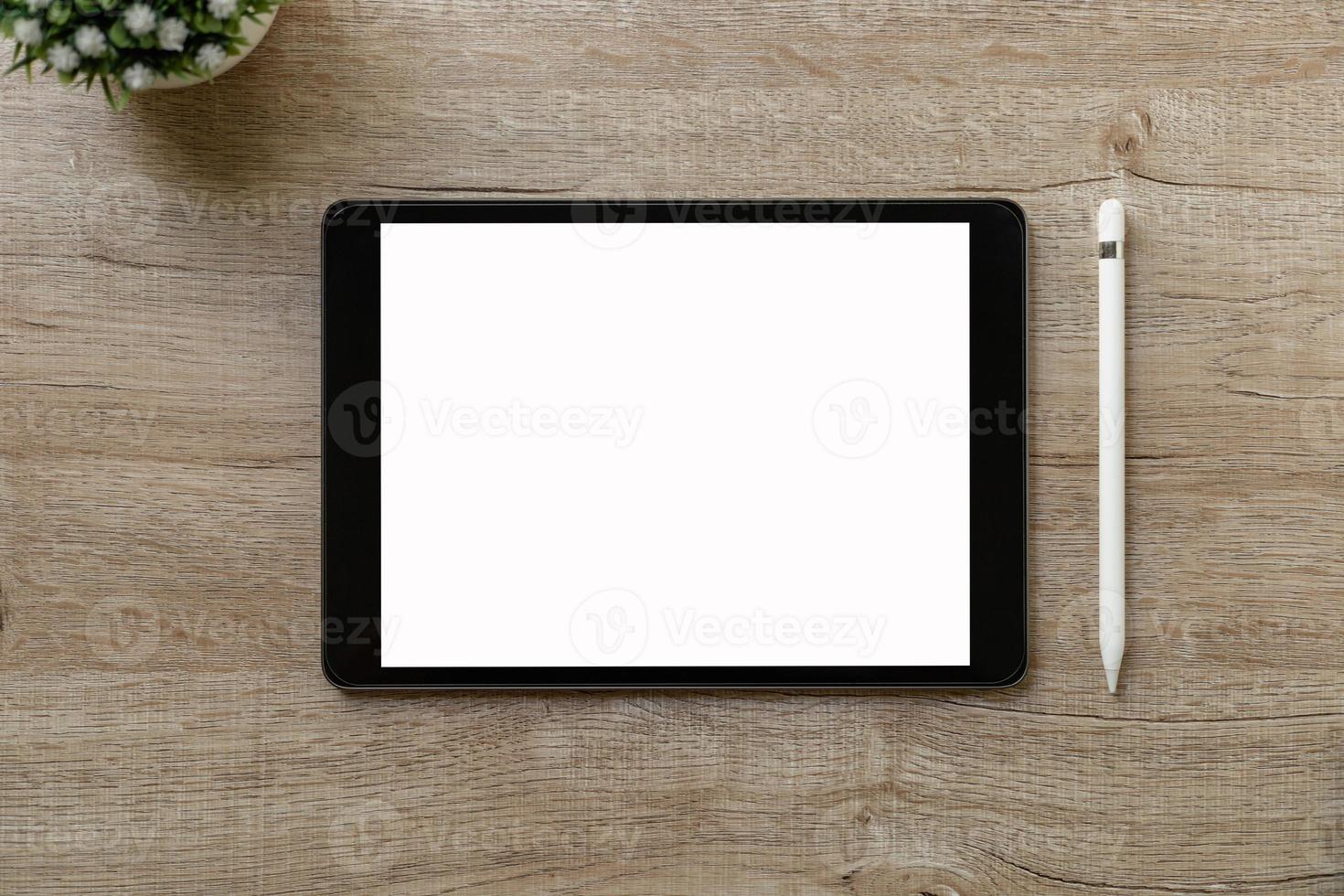 Black tablet with white blank screen is on top of brown paper with supplies. Top view, flat lay. photo