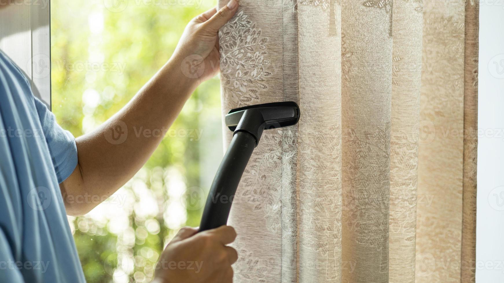 man dry cleaning curtain with vacuum cleaner. in living room at home. photo