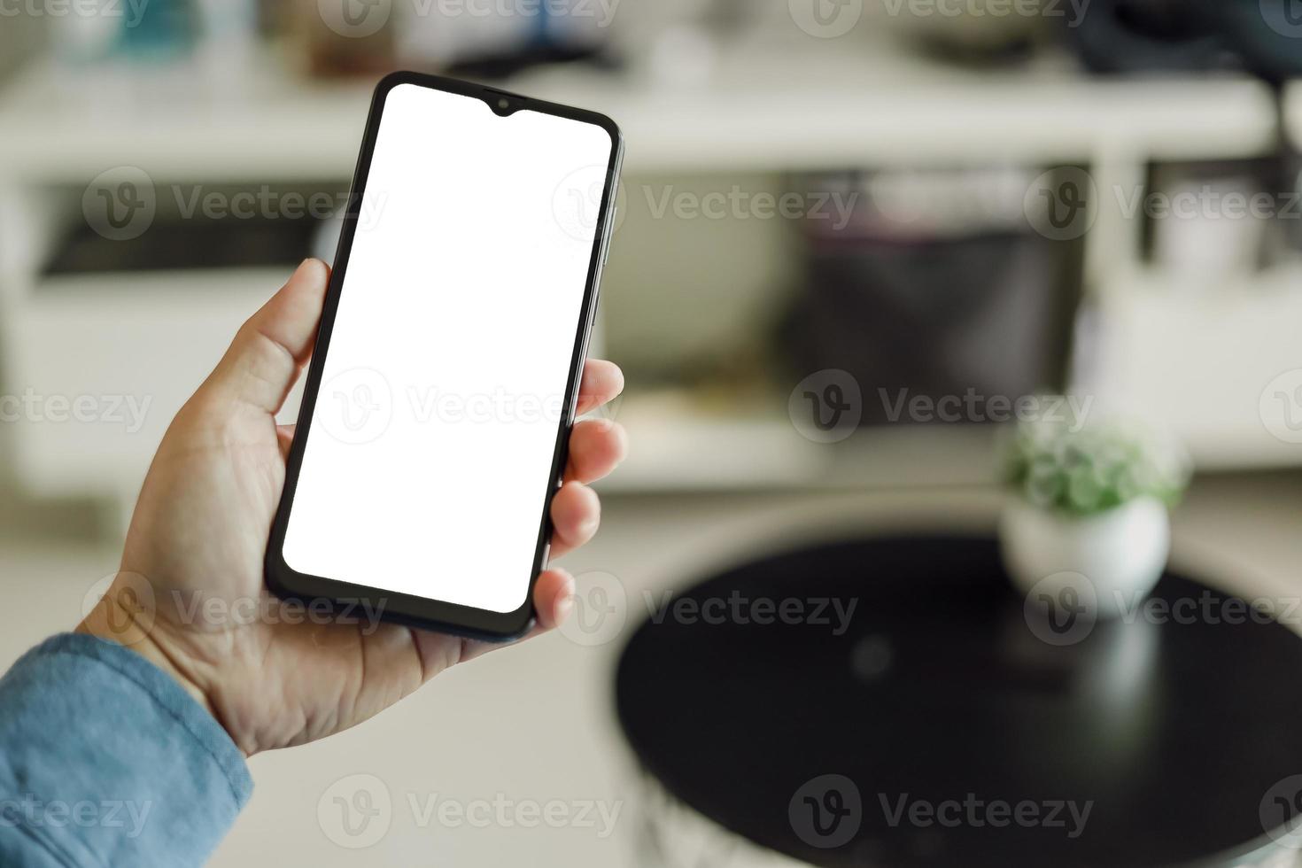 Mockup image of a man holding black mobile phone with blank white screen. In living room at home. photo