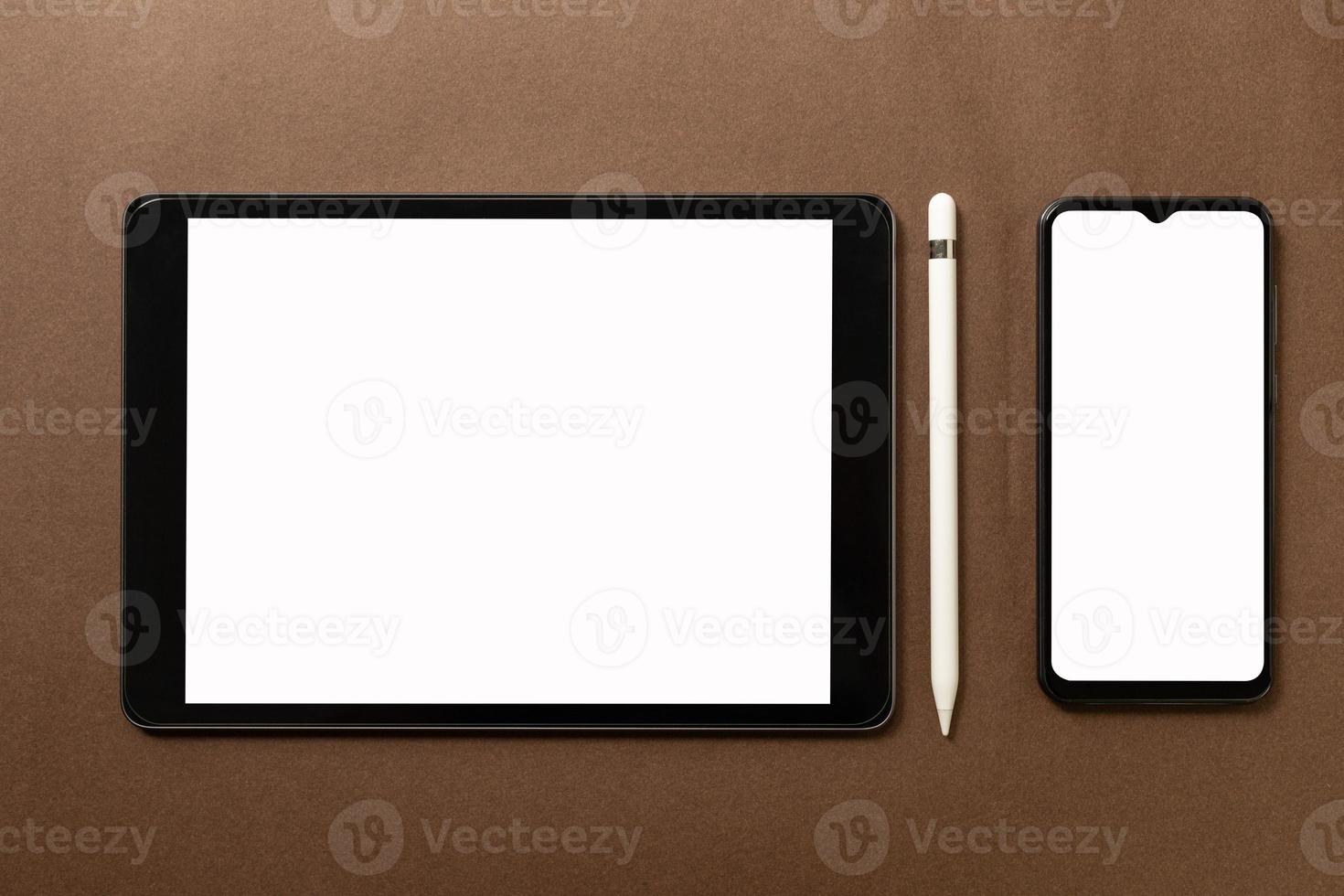la tableta negra con pantalla blanca en blanco está sobre papel marrón con suministros. vista superior, endecha plana. foto