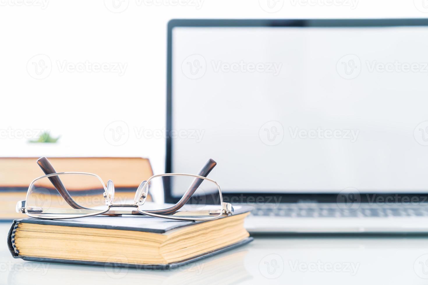 Glasses on book with blank screen laptop computer on deck photo