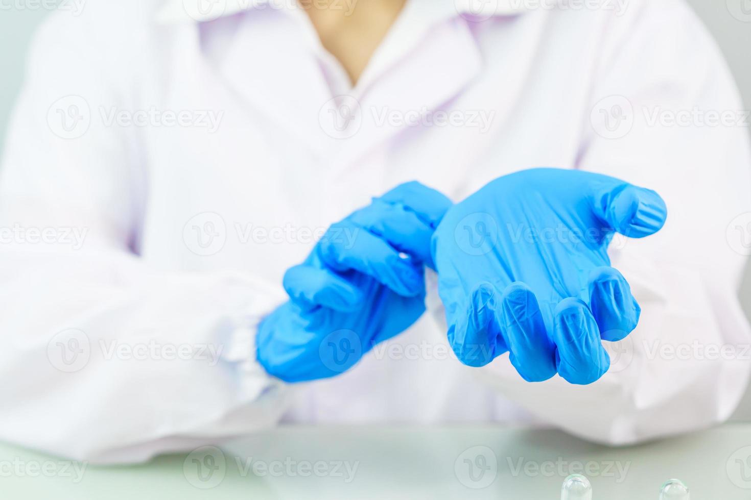 Manos científicas poniéndose guantes de látex azul de nitrilo en una bata de laboratorio usando guantes de nitrilo foto