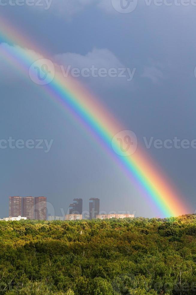 arco iris en el cielo gris sobre la ciudad y los árboles verdes foto