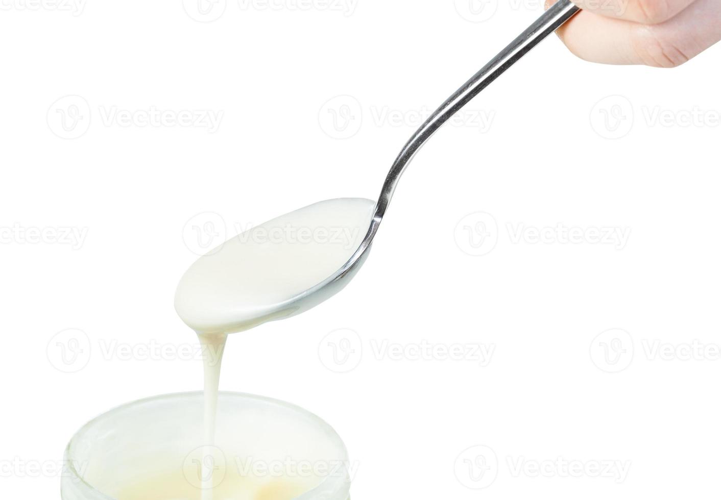 white honey pouring from steel spoon in glass jar photo