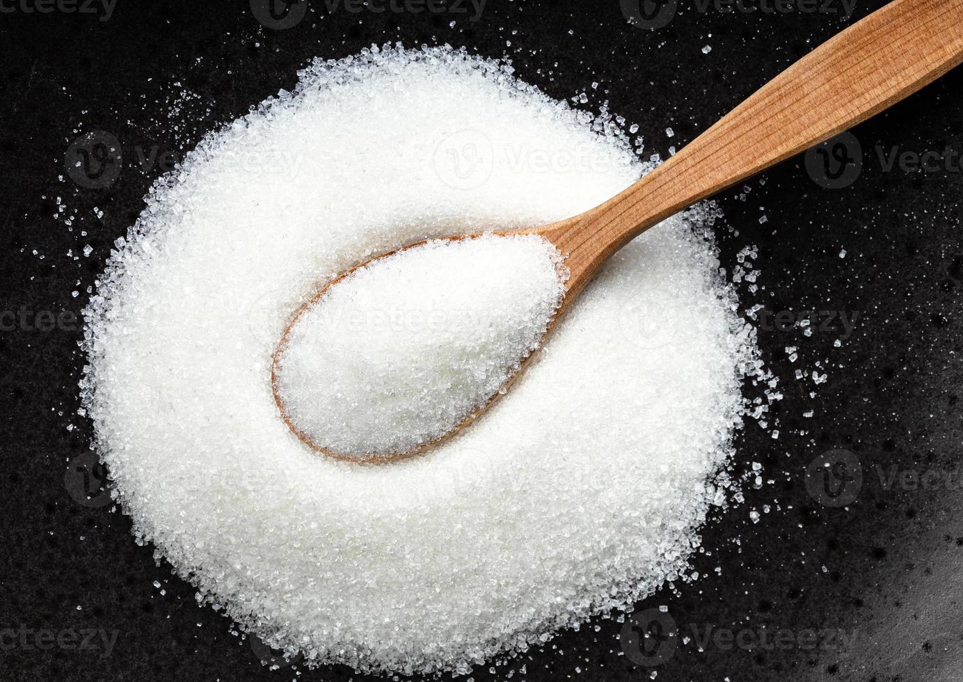 top view spoon with white refined sugar on black photo