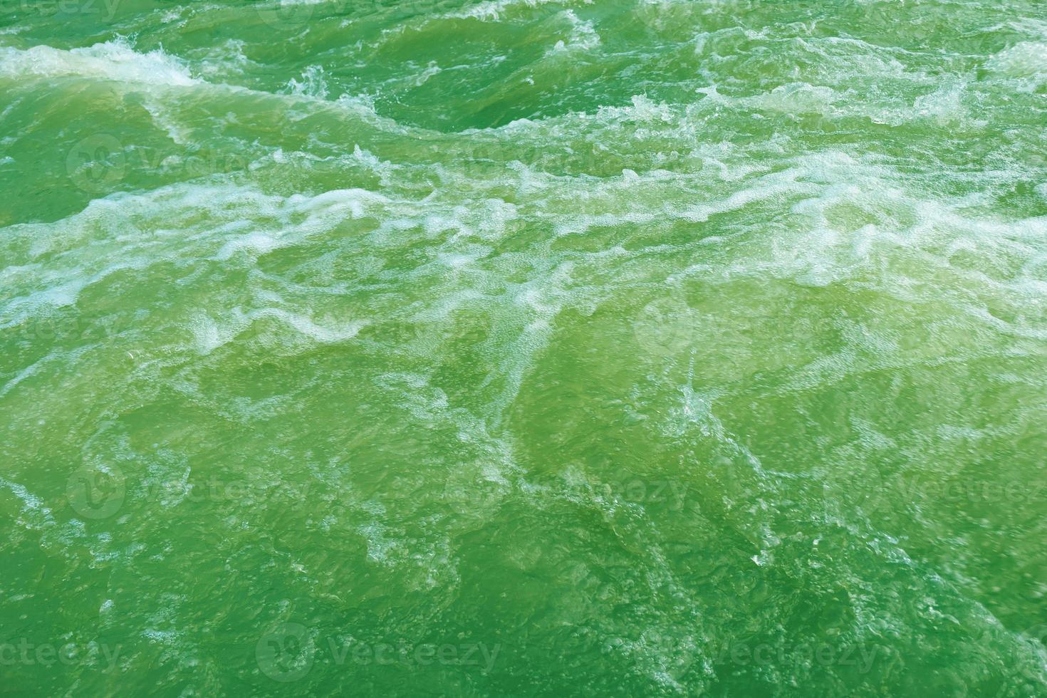 Defocus blurred transparent green colored clear calm water surface texture with splash, bubble. Shining green water ripple background. Surface of water in swimming pool. Green bubble water, splash. photo
