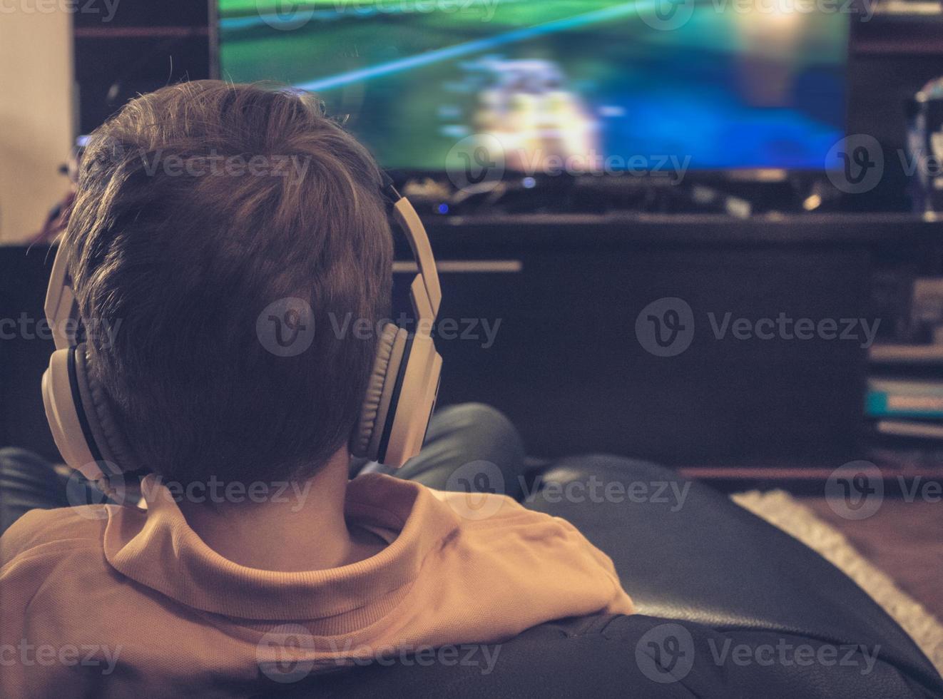 Rear view of boy with headphones watching TV at home. photo