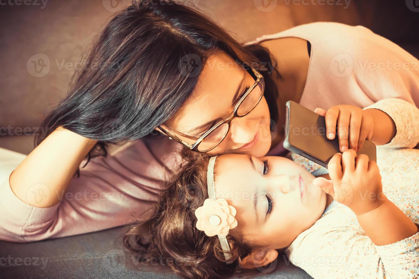 Happy mother and daughter watching cartoons on smart phone. photo