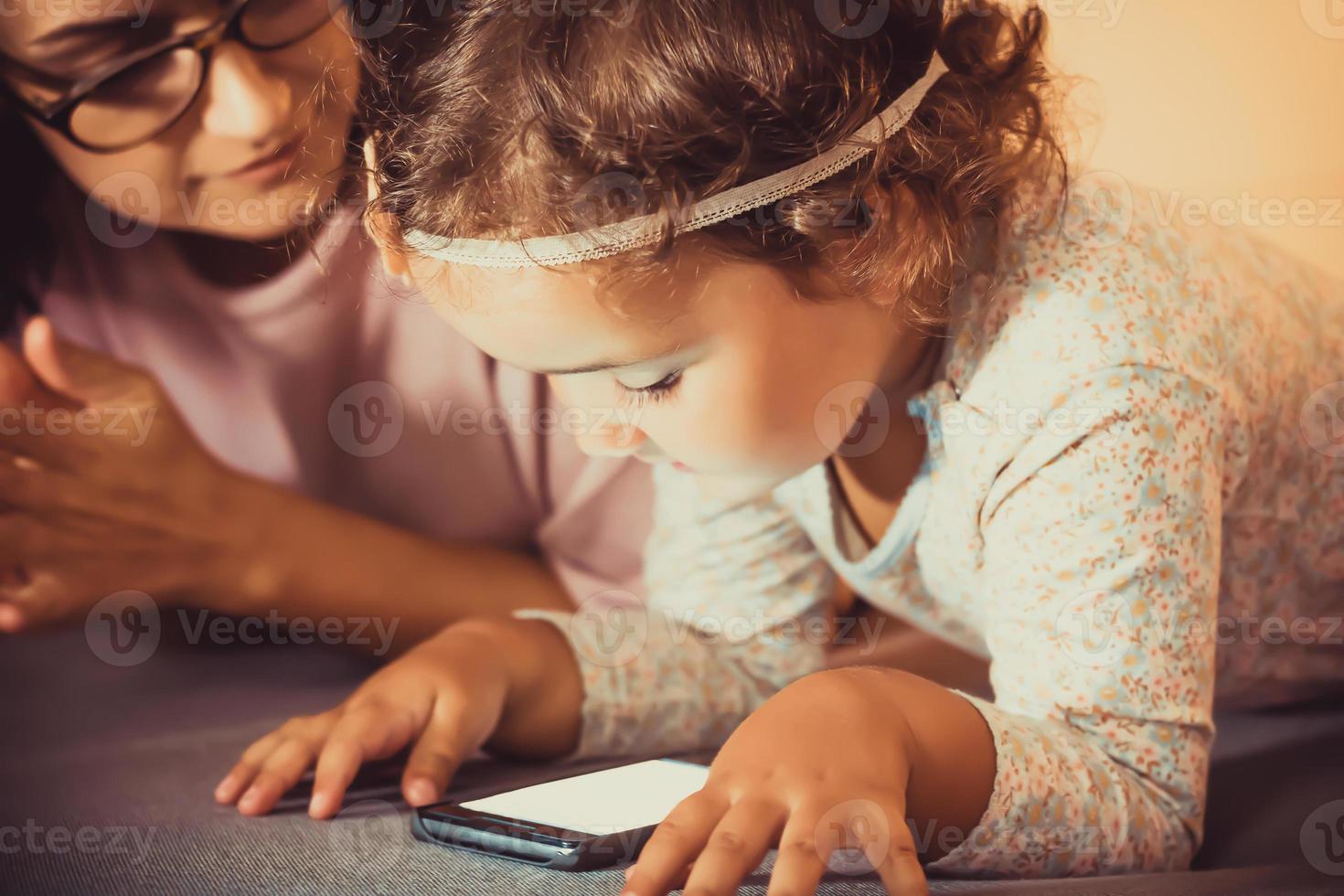 Little girl using smart phone while being with her mother at home. photo
