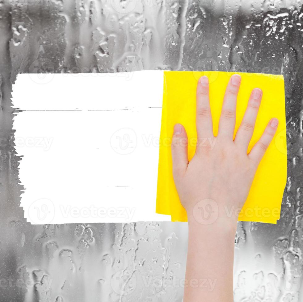 hand deletes rainy water on window by yellow rag photo