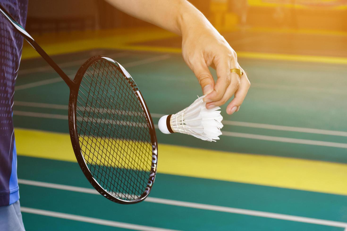 Badminton racket and old white shuttlecock holding in hands of player while serving it over the net ahead, blur badminton court background and selective focus photo