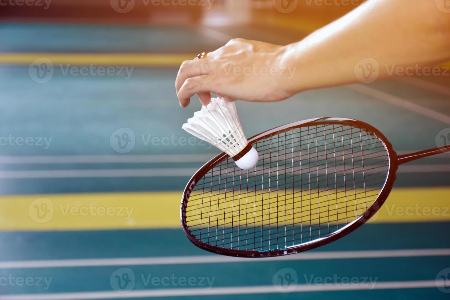 Badminton racket and old white shuttlecock holding in hands of player while serving it over the net ahead, blur badminton court background and selective focus photo