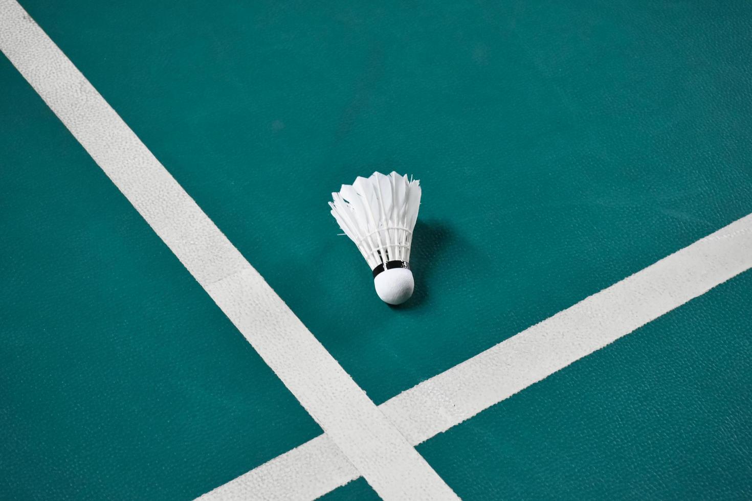 volante de bádminton blanco crema en el suelo verde en la cancha de bádminton cubierta, fondo de bádminton borroso, espacio de copia foto