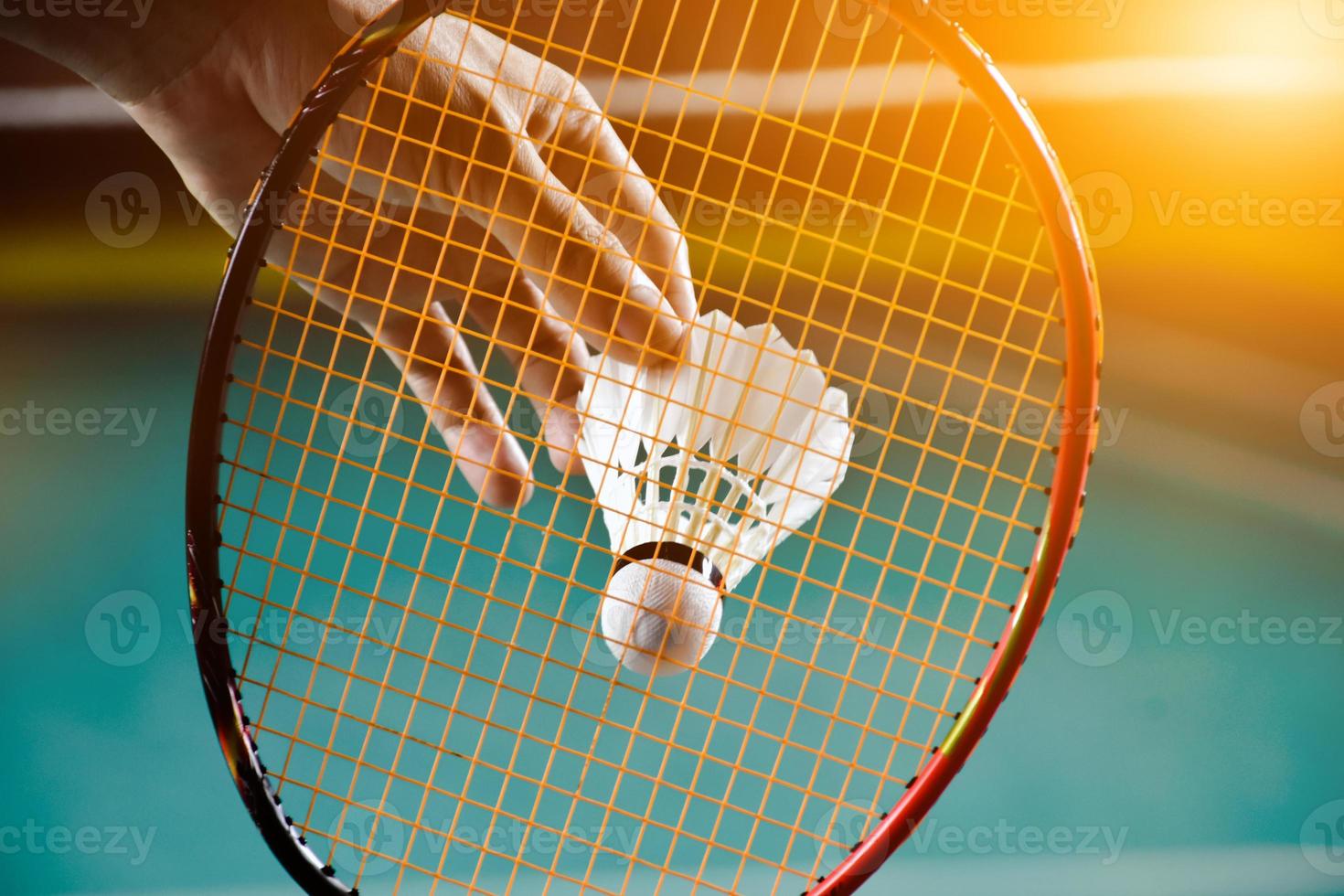 Badminton racket and old white shuttlecock holding in hands of player while serving it over the net ahead, blur badminton court background and selective focus photo