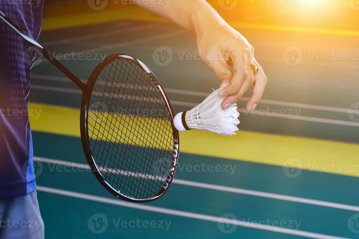 Badminton racket and old white shuttlecock holding in hands of player while serving it over the net ahead, blur badminton court background and selective focus photo