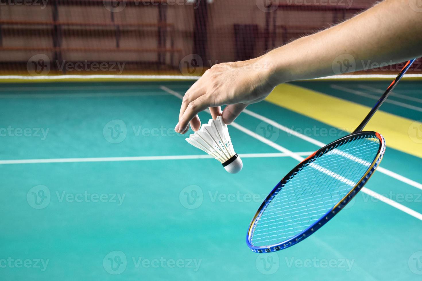 Badminton racket and old white shuttlecock holding in hands of player while serving it over the net ahead, blur badminton court background and selective focus photo