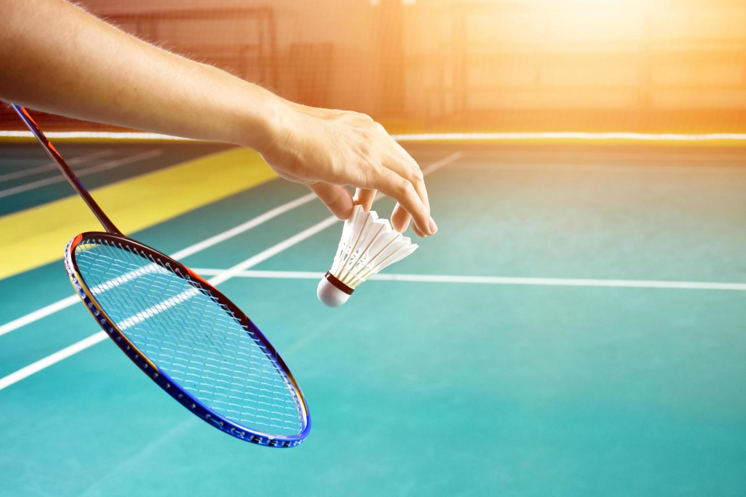 Badminton racket and old white shuttlecock holding in hands of player while serving it over the net ahead, blur badminton court background and selective focus photo