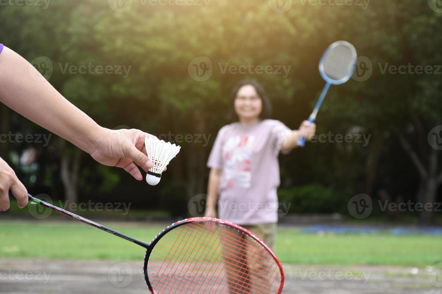 juego de bádminton al aire libre, enfoque suave y selectivo en el volante blanco, fondo asiático borroso de mujeres y árboles, concepto de juego de bádminton al aire libre en tiempos libres y actividad diaria. foto