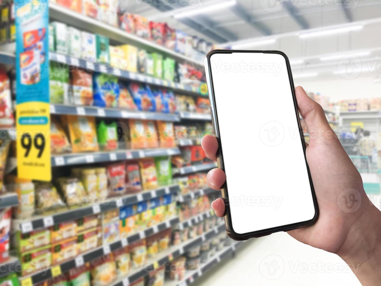 Smart shopping concept mobile phone in hand in front of goods shelves in supermarket and grocery store. blank white screen mockup for your own creativity. photo